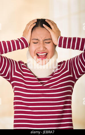 Young hispanic woman posing for camera wearing neck brace, montrant des signes de moment douloureux avec le langage du corps, blessure concept. Banque D'Images