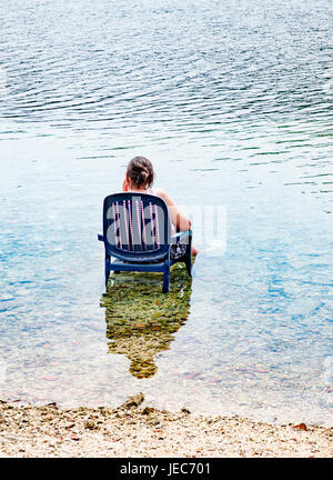 Une femme cools off à la plage un jour chaud par assis dans une chaise avec ses pieds dans la mer - Croatie Banque D'Images