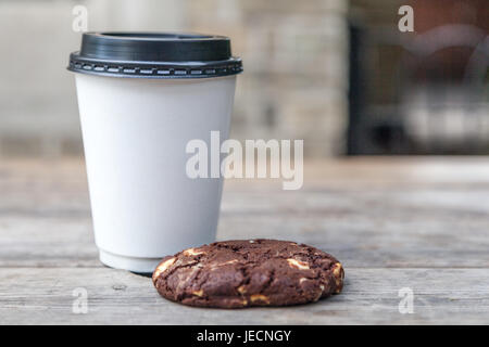 Tasse à emporter blanc avec pas de logo et d'un biscuit aux brisures de chocolat sur une table à l'extérieur Banque D'Images