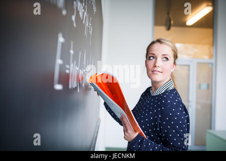 Jolie jeune étudiant écrit sur le tableau/blackboard pendant un cours de mathématiques. Banque D'Images