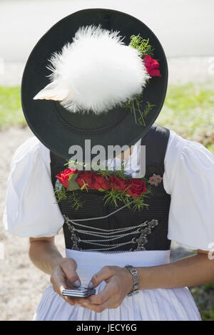 Germany, Bavaria, Burghausen, procession, jeune femme en costume national traditionnel avec un téléphone mobile, la moitié, portrait Banque D'Images