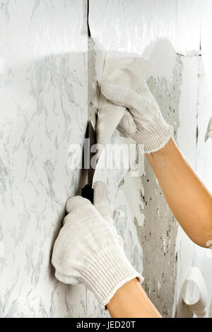 Mains en éliminant l'ancien papier peint de mur à l'aide d'une spatule pour la réparation Banque D'Images