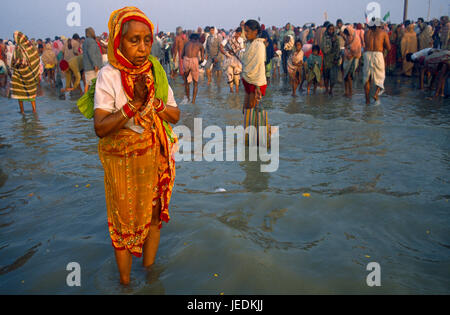 L'Inde, le Bengale occidental, Sagar, Sagar pèlerins Festival femme âgée porter du rouge et jaune sari priant dans l'eau en premier plan. Banque D'Images