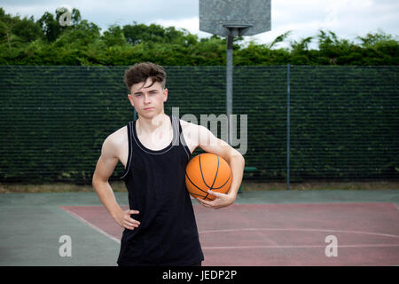 Teenage boy holding a basketball sur une cour Banque D'Images