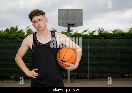 Teenage boy holding a basketball sur une cour Banque D'Images