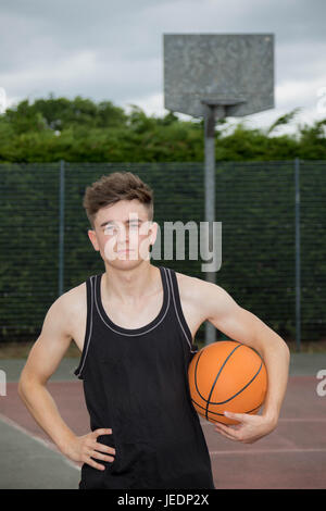 Teenage boy holding a basketball sur une cour Banque D'Images