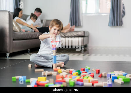 Asian boy jouer jouet en bois dans la salle de séjour avec le père, la mère et la fille en arrière-plan. Famille heureuse. Banque D'Images