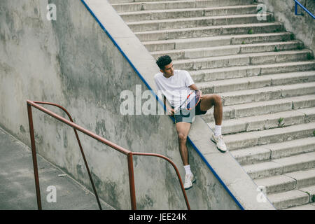 Un athlète avec une raquette de tennis est situé sur une rampe en béton d'étapes. Banque D'Images