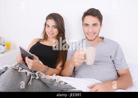 Belle jeune couple having breakfast in bed and using digital tablet. À l'intérieur. Banque D'Images