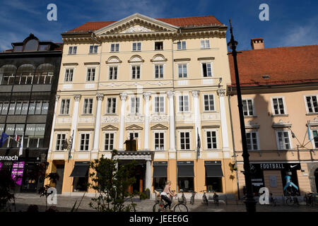 Femme sur vélo à Ikona immeuble sur la rue pavée de la vieille ville Town Square en face de l'hôtel de ville Ljubljana Slovénie Europe Banque D'Images