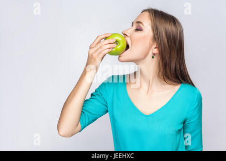 Belle jeune femme avec des taches de rousseur et robe vert pomme exploitation et de manger avec les yeux fermés. studio shot, isolé sur fond gris clair. Banque D'Images