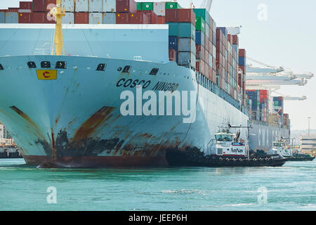 Le porte-conteneurs COSCO Géant Ningbo est guidée dans Quai J270 sur Pier J par deux remorqueurs du tracteur au terminal à conteneurs de Long Beach, Los Angeles, USA. Banque D'Images