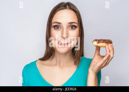 Portrait de belle fille avec des beignets au chocolat. enjoing et looking at camera avec la langue. studio shot sur fond gris clair. Banque D'Images