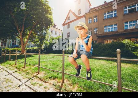 Journée d'été dans la ville. Petit garçon avec hat eating big glace sur la rue. Banque D'Images