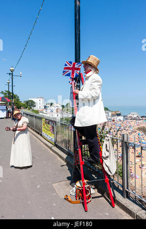 M. William Thompkins, Lamplighter, Charles Dickens caractère, histoire. Vêtu de blanc manteau et chapeau de paille, se dresse sur l'échelle contre la lumière avec Union Jack. Banque D'Images