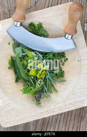 Demi-lune Mezzaluna herb chopper et chopping board une sélection d'herbes. UK Banque D'Images