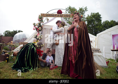 Fi Sexton, 32 et Peter Howe, 38 ans, tous deux de Londres accompagné par son fils Thomas Howe, 2 prendre part à une cérémonie de mariage Mariage. La cérémonie réalisée par Glenda proctor (Brown) et Jane Tove (vert) impliqués attacher leurs mains ensemble avec les obligations, sautant d'un balai et de manger un gâteau et de boire ale ensemble au festival de Glastonbury, à la ferme digne dans le Somerset. Banque D'Images