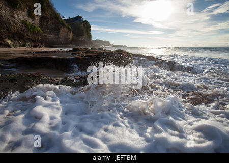 Océan vagues avec mousse de battre contre les rochers au coucher du soleil Banque D'Images