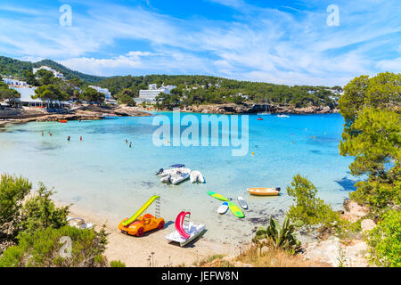 Green pine tree on cliff rock donnant sur la magnifique baie de Cala Portinatx avec planches et canot bateaux sur la mer d'azur de l'eau, l'île d'Ibiza, Espagne Banque D'Images