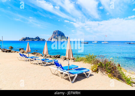 Des chaises longues avec parasols sur la plage de Cala d'Hort avec belle mer bleu azur et de l'eau Es Vedra île dans la distance, l'île d'Ibiza, Espagne Banque D'Images