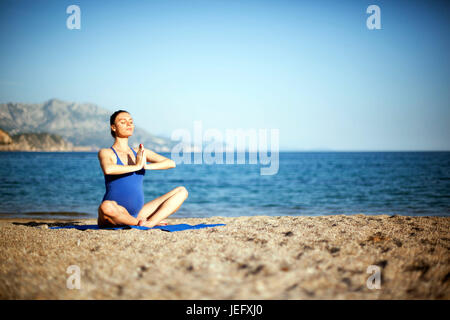 Jeune femme enceinte dans la méditation de yoga on beach Banque D'Images