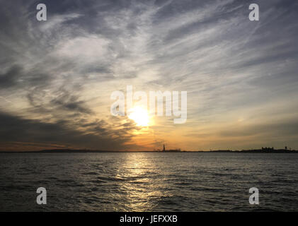 Statue de la liberté sur Liberty Island dans le port de New York au coucher du soleil. Ciel spectaculaire avec nuages dynamiques au coucher du soleil. Statue de la liberté au loin Banque D'Images