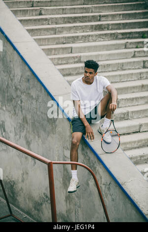 Un athlète avec une raquette de tennis est situé sur une rampe en béton d'étapes. Banque D'Images