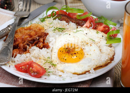 Le petit déjeuner - riz bouilli avec des œufs brouillés, bacon, les tranches de tomate et les verts Banque D'Images