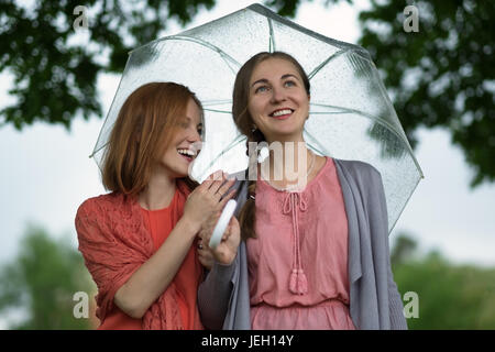 Deux femmes marchant park dans la pluie et de parler. L'amitié et les gens de la communication. Banque D'Images