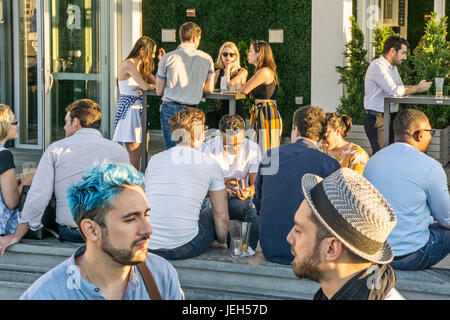 Divers groupes de jeunes dorés par coucher de soleil profitez de la socialisation dont couple gay, l'un avec coloration bleu dans ses cheveux Ink48 Hotel bar sur le toit Banque D'Images