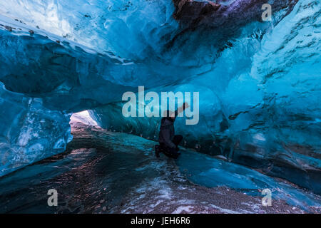 Un homme examine la glace bleue claire à l'intérieur d'un tunnel sous la surface de Black Rapids Glacier en hiver ; Alaska, États-Unis d'Amérique Banque D'Images