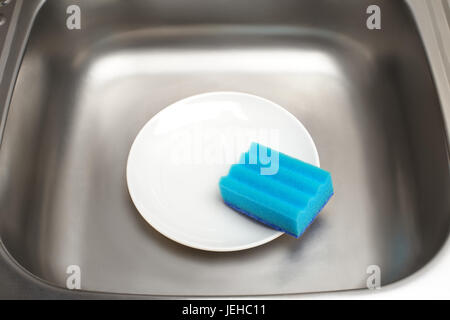 Close up d'évier de cuisine avec plaque blanche et bleu éponge de nettoyage Banque D'Images