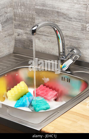 Close up d'évier de cuisine pleine de mousse avec l'eau du robinet, bleu, rose, jaune et vert, les éponges de nettoyage Banque D'Images