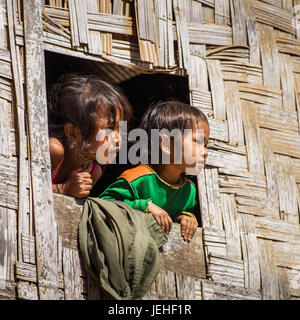 Un jeune garçon et fille se pencher à l'une fenêtre d'un immeuble avec une façade tissée, Kamu village ; Tambon Po Chang, Wat Chiang Rai, Thaïlande Banque D'Images