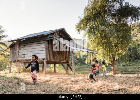 Les jeunes enfants jouer ensemble à côté d'une maison en bois sur pilotis ; Province de Luang Prabang, Laos Banque D'Images