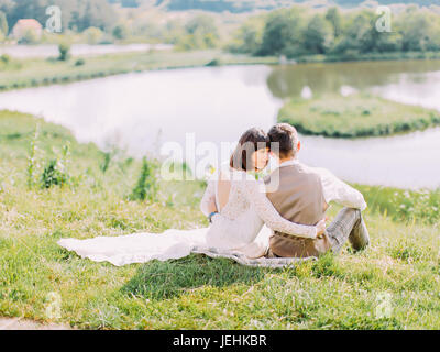 Hugging couple est assis sur l'herbe et profiter de la nature. La vue arrière. Banque D'Images