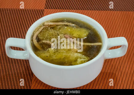 La tasse en céramique blanche de délicieux maw de poisson braisé chinois dans une soupe de sauce rouge sur un plat rouge. Banque D'Images