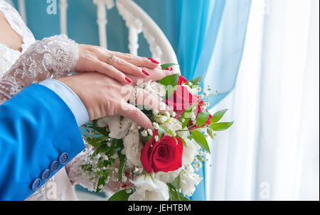 Deux mains suite nuptiale dans une robe blanche et un costume bleu, allongé sur le bouquet de roses rouges. Banque D'Images