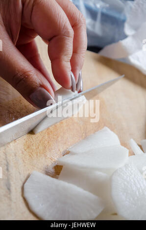 Une femme radis blanc côtelettes dans une cuisine avec un couteau bien aiguisé sur une planche à découper en bois. Banque D'Images