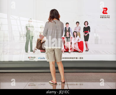 PÉKIN-AOÛT. 30, 2010. Fille devant un panneau d'affichage à l'aéroport international de Beijing Capital. Le marché chinois de la publicité extérieure a connu une croissance énorme. Banque D'Images