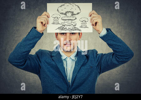 Young businessman holding a white paper sur sa tête avec un dessin d'explosion , isolé sur fond de mur gris.L'état mental de la dépression. Banque D'Images