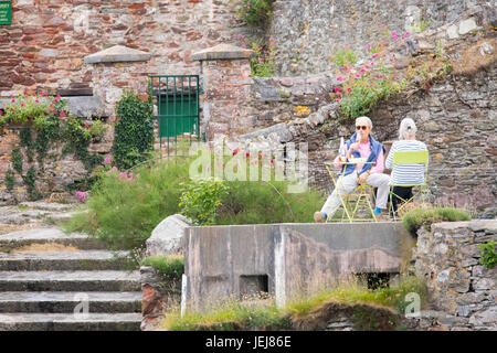 Un homme et femme couple buvant un verre de vin un ils sont assis sur des chaises dans leur jardin donnant sur le port de la station balnéaire populaire de village à Kingsand Cornwall au cours d'une soirée d'été Banque D'Images