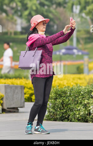 PÉKIN-28 AVRIL 2016. Une femme à la mode d'âge moyen prend selfie avec son smartphone dans un parc, le temps ensoleillé. Banque D'Images