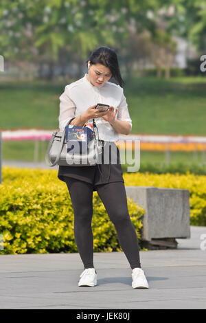 PÉKIN-28 AVRIL 2016. Jolie jeune fille chinoise dans le parc occupé avec son téléphone une journée ensoleillée. Banque D'Images