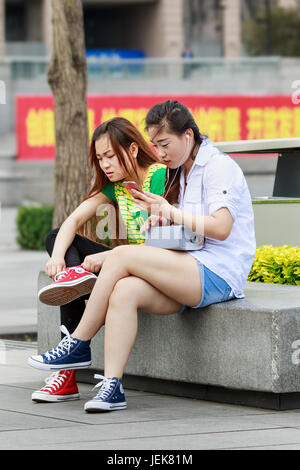 PÉKIN-4 MAI 2016. Deux jeunes filles chinoises assis dans un parc occupé avec leur smartphone. Banque D'Images