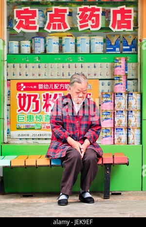 KUNMING-2 JUILLET 2014. Femme aînée ayant une sieste devant un magasin de pharmacie. La population âgée de la Chine (60 ans ou plus) est d’environ 128 millions. Banque D'Images