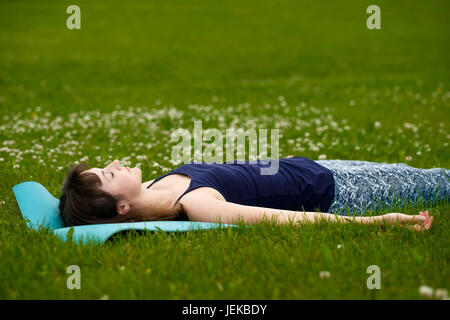 Girl doing yoga, méditation, cadavre ou Shavasana en position park on Green grass Banque D'Images