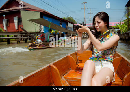 Marché flottant de Damnoen Saduak touriste. Jeune voyageur woman holding camera sitting in canal ferry, Beautiful happy smiling mixed race chinoise asiatique w Banque D'Images