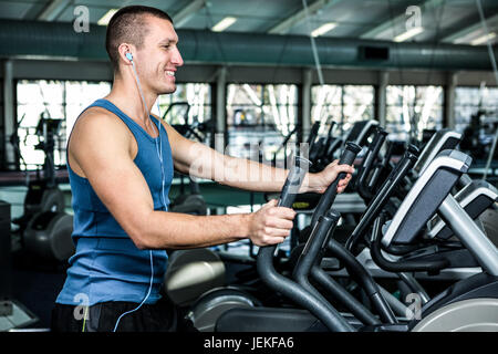 Homme musclé sourire à l'aide d'une machine elliptique Banque D'Images