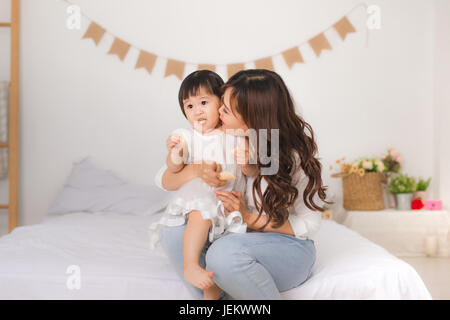 Heureux famille aimante. Mère et fille enfant s'amusent sur le lit tandis que baby eating snack Banque D'Images